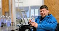 Mann in blauem Kapuzenpullover hält klare Wasserflasche in Produktionsumgebung