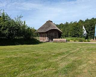 Kleines Holzhaus mit Reetdach in einer grünen Landschaft und blauem Himmel