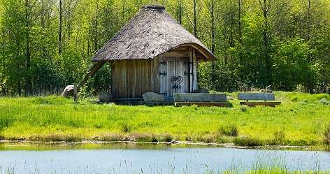 Traditionelle Hütte neben einem ruhigen Teich in der Natur.